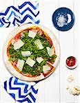 Overhead View of Pizza on Wooden Cutting Board with Bowl of Chili Sauce, Garlic Cloves, Dish with Salt, and Napkin