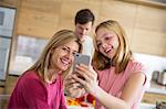 Mid adult woman and daughter taking smartphone selfie in dining room