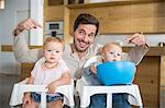 Father pointing at male and female twin toddlers in high chairs