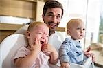 Father between male and female twin toddlers in high chairs