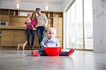 Family watching male toddler with bowl on dining room floor