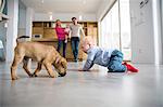 Male toddler playing with puppy on dining room floor