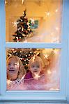 Sisters looking out of window with Christmas decorations