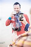 Couple outdoors, drinking wine, woman taking photograph of man