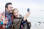 Couple on beach, drinking wine, taking self portrait using smartphone