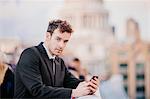 Businessman texting on smartphone whilst leaning on millennium bridge, London, UK