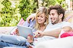 Couple sitting on vintage sofa in garden using digital tablet