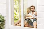 Mid adult couple sitting on floor using digital tablet at house window