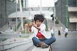 Young woman taking smartphone selfie whilst sitting on shopping center wall