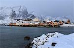 Snowy peaks and rorbu, the red houses of fishermen, in the landscape of the Lofoten Islands, Arctic, Norway, Scandinavia, Europe