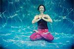 Mature woman wearing red yoga pants and vest, in yoga position, underwater view