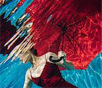 Mature woman wearing red dress, holding red umbrella, underwater view, mid section