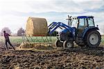 Boy farmer removing netting from hay stack in dairy farm field