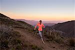 Rear view of young woman trail running down dirt track at dusk on Pacific Crest Trail, Pine Valley, California, USA