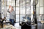 Young male vodka distiller measuring liquid in cylinder in distillery workshop