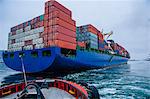 Tugboat manoeuvring container ship on river, Tacoma, Washington, USA