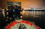 Tugboat manoeuvring cargo ship in harbor at night, Tacoma, Washington, USA