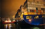 Tugboat manoeuvring container ship on river at night, Tacoma, Washington, USA