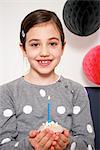 Girl on birthday party holding cupcake with burning candle, Munich, Bavaria, Germany