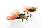 Culinary food. Prosciutto slices with black olives and fresh herbs in white bowl isolated on white background.