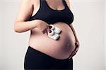 Pregnant woman showing her belly and the baby socks, over a gray background