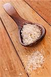 Sea salt crystals on wooden spoon on wooden background. Culinary high quality cooking salt.