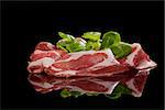 Delicious prosciutto slices with green corn salad isolated on black background. Culinary traditional italian ham.