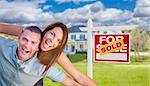 Playful Excited Military Couple In Front of Home with Sold Real Estate Sign.