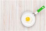 Fried egg in a frying pan. Top view over white wooden table with copy space