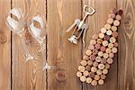 Wine bottle shaped corks, glasses and corkscrew over rustic wooden table background. View from above