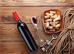 Red wine bottle, wine glass, bowl with corks and corkscrew. View from above over rustic wooden table background