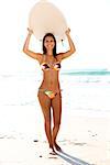 A beautiful surfer girl at the beach holding up her surfboard