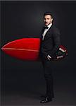 Studio portrait of a fashion young man wearing a suit and posing with a surfboard