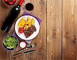 Steak with grilled potato, corn, salad and red wine over wooden table. Top view with copy space