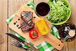 Steak with grilled corn, salad and red wine over wooden table. Top view