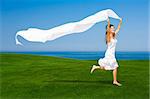 Beautiful woman running and jumping on a green meadow with a white tisue