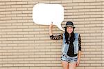 Beautiful and young teenager holding a thought balloon, in front of a brick wall