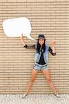 Beautiful and young teenager holding a thought balloon, in front of a brick wall