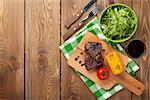 Steak with grilled corn, salad and red wine on wooden table. Top view with copy space