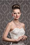 very pretty woman with elegant style. Wearing white decorated dress, pearls necklace and classic hairdo. Looking in camera and smiling with calm expression