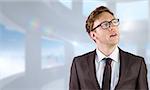 Young businessman thinking and looking up against bright white room with windows