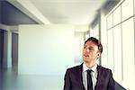 Young businessman thinking and looking up against white room with screen