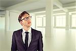 Young businessman thinking and looking up against white room with windows