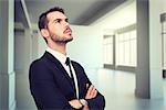 Thinking businessman with his arms crossed against white room with screen