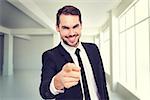 Happy businessman pointing at camera against white room with windows