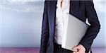 Businesswoman holding laptop against clouds in a room