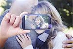 Hand holding smartphone showing against cute woman smiling at camera with her boyfriend