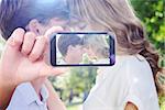 Hand holding smartphone showing against cute couple facing each other in the park