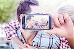 Hand holding smartphone showing against man giving his pretty blonde girlfriend a piggy back