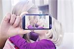 Hand holding smartphone showing against happy mother and daughter on the couch